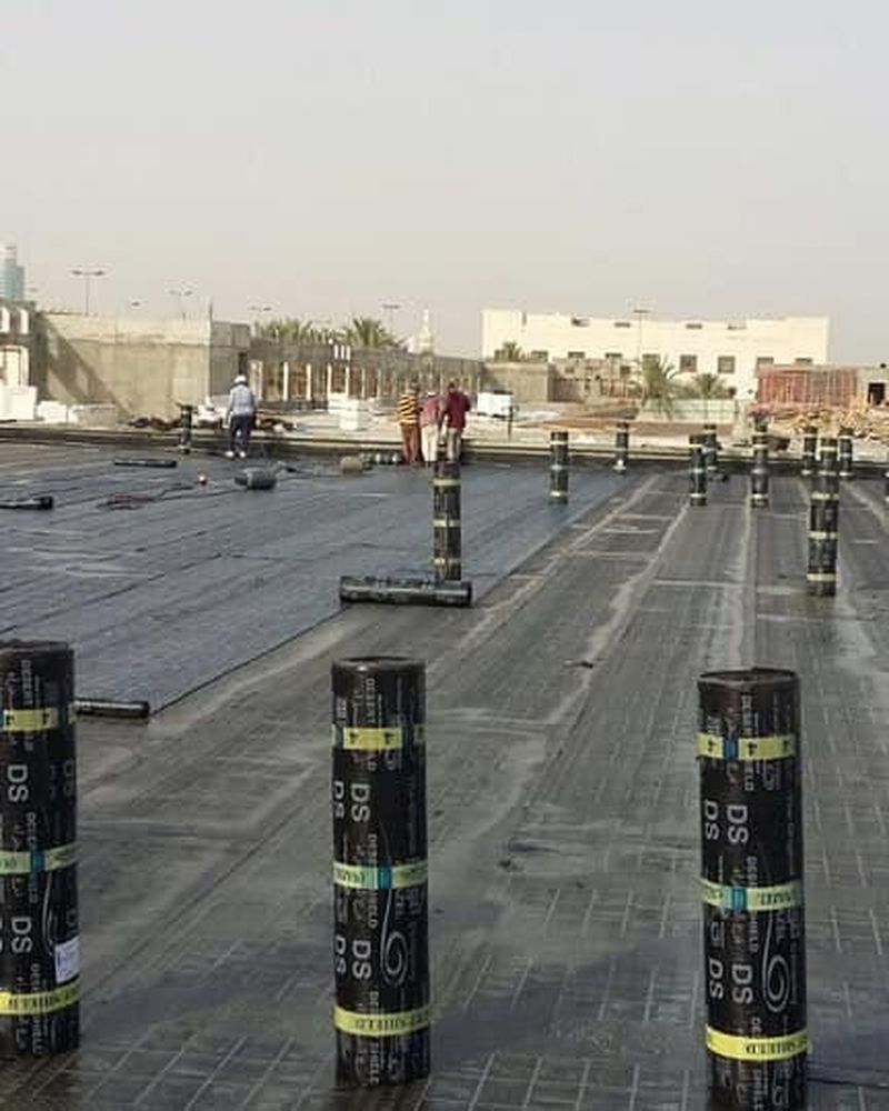 توزيع لفائف العزل البيتوميني على سطح مبنى في الكويت استعداداً للتركيب